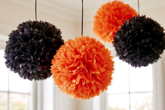 Halloween tissue paper pom-poms in orange and black (three), hanging from ceiling, white background, bright light, party decoration
