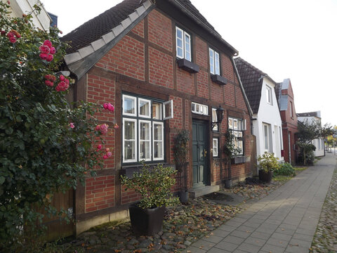 Traditional historic half-timbered house with a red brick facade, dark wooden beams, white-framed windows and blooming roses on a quiet residential street in a German town. 