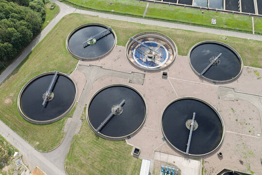 Aerial view of a water treatment plant featuring five large circular sedimentation tanks with rotating arms surrounded by grassy areas in the United Kingdom.