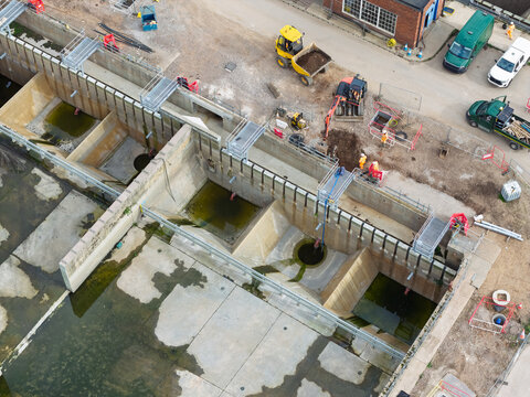 Aerial view of water treatment facility with concrete basins, construction machinery, and workers in the United Kingdom.