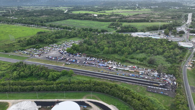 Aerial view of Arecibo Motorsports drag strip with parked cars, spectators, and surrounding lush green landscape in Cambalache, Arecibo, Puerto Rico.