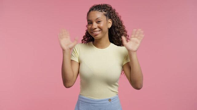 Welcoming teenage girl waving hand - hello, salute, chao, hola. Parting, say bye to camera. Beautiful young woman on pink studio background
