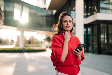 Professional businesswoman with smartphone standing confident in city against modern corporate...