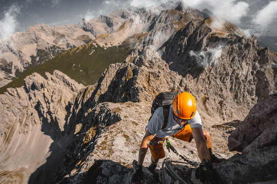 Close-up of a focused solo male climber ascending a rugged rock wall on a via ferrata in the Austrian Alps near Innsbruck, using safety equipment and climbing gear.