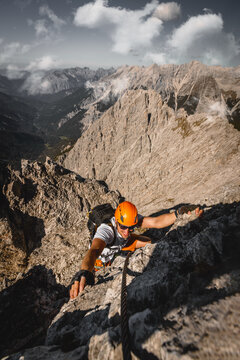 Close-up of a focused solo male climber ascending a rugged rock wall on a via ferrata in the Austrian Alps near Innsbruck, using safety equipment and climbing gear.