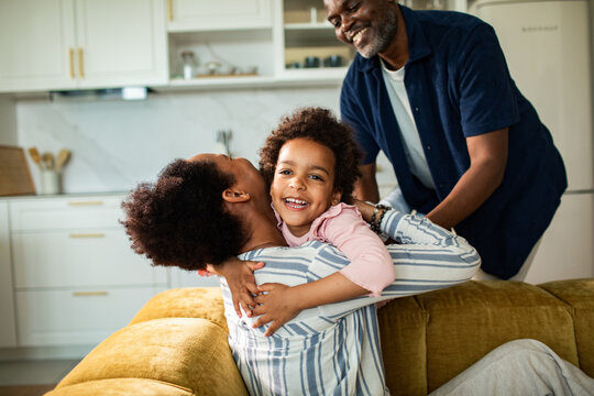 Smiling child hugs parent on couch while father looks on