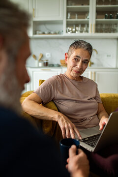 Older woman using laptop while talking with partner at home