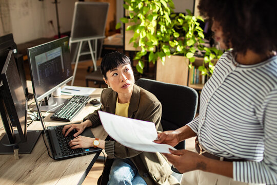 Woman at desk receives document from coworker in office