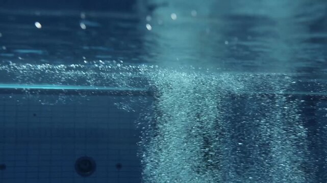 Underwater POV looking toward the surface of an Olympic swimming pool as air bubbles rise past the camera and diving platforms come into view.