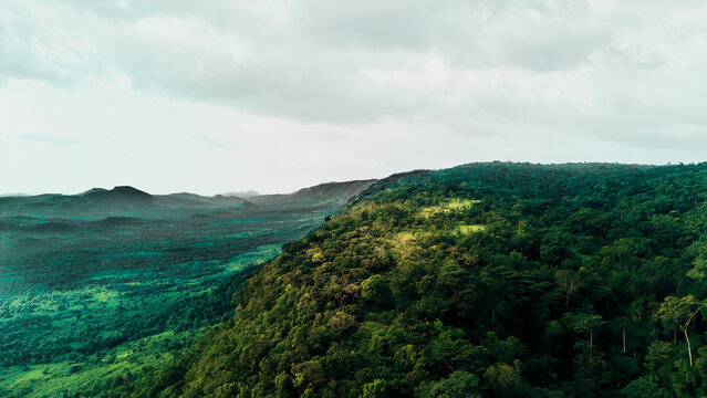 Aerial view of the lush green hills and dense forest landscape surrounding the Erin Ijesha Waterfall under a cloudy sky in Erin-Ijesa, Osun, Nigeria.