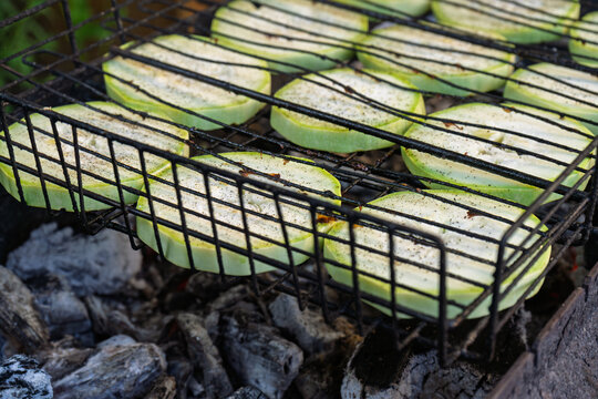 Fresh zucchini slices cooking in grill basket over hot charcoal