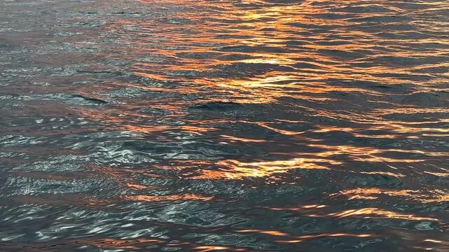 Glowing sparkling sun reflections on rippled wavy sea surface, sunset glow and waves on water, evening setting sun at seaside, sunlight covering edges of waves, golden light reflecting at sunset sea.