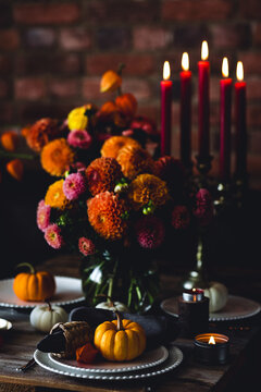 Fall table decoration with pumpkin centrepiece composition. Family cozy thanksgiving dinner arrangement indoors, elegant wedding decor. Countryside style, candle light, autumn mood. Dark background