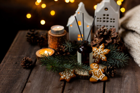 Scented aromatic candles on wooden table, liquid reed diffuser with sticks with pine, spruce, cedar, gingerbread cookies scent. Xmas spirit, creating holiday atmosphere, festive mood at home