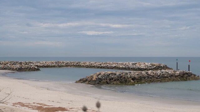 Rock breakwater arms forming a sheltered harbour entrance at West Beach, Adelaide, South Australia, with channel marker poles. Coastal protection and marine infrastructure, safe boating access.