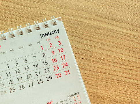 Close up of a desk calendar 2027 open to January on a wooden background with intentionally blurred numbers and copy space for planning, grainy film texture, high quality photo