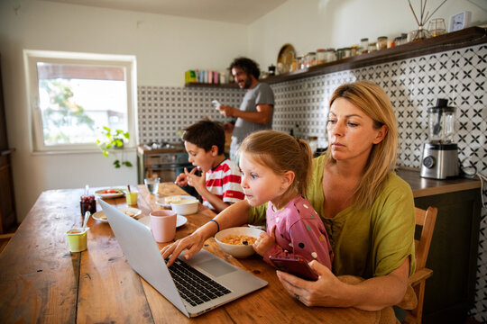 Mother working from home with daughter at breakfast