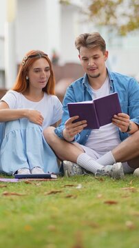 Young couple reading a book together on university campus grass