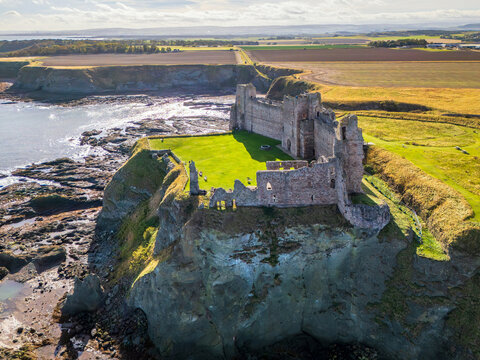 Aerial view of Tantallon Castle ruins perched on a cliffside overlooking the North Sea, with green grass and stone walls in North Berwick, Scotland, United Kingdom.
