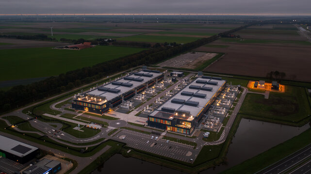 Aerial view of a modern data center facility with industrial buildings, parking areas, and surrounding agricultural fields in The Netherlands.