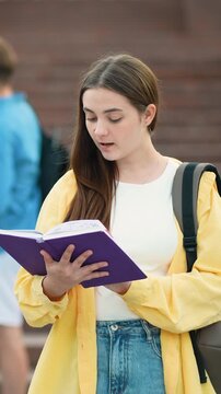 Young female student reading book outdoors