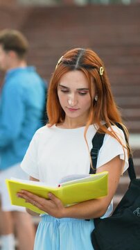 Young female student with red hair reading a book