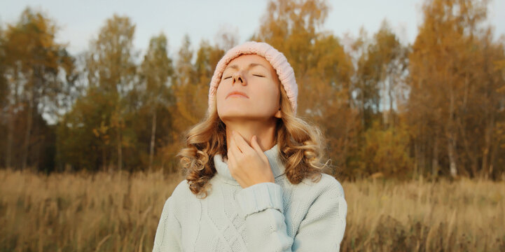 Sick woman suffering from acute sore in throat flu, touches neck with hand outdoor in park
