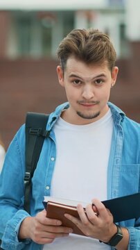 Young male university student reading book outside campus
