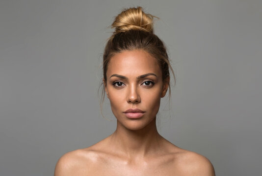 Studio beauty portrait of a woman with hair in a bun and bare shoulders against a grey background[cite: 14].