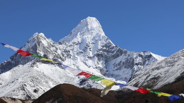 Colorful Buddhist prayer flags flutter in the Himalayan breeze with majestic Ama Dablam rising in the background. Vibrant fabric banners contrast beautifully against snow-covered peaks