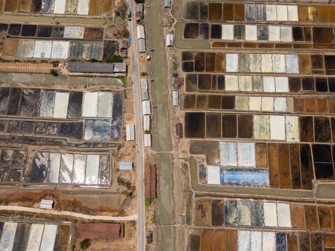 Aerial view of Sentra Garam Jepara, featuring rectangular salt evaporation ponds with varying water levels, separated by narrow paths and a road in Kecamatan Kedung, Jawa Tengah, Indonesia.