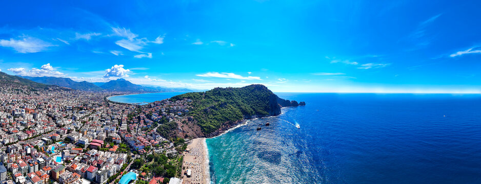 Panoramic aerial view of Alanya town, green peninsula, Cleopatra beach, Taurus mountains and blue Mediterranean sea in Antalya, Turkey. Sunny summer day, urban architecture, coastline and horizon.