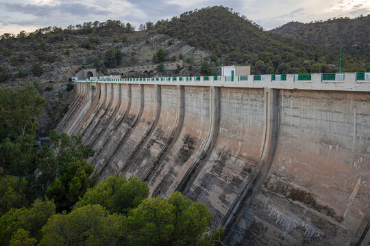 Wide shot of Amadorio Dam with curved concrete structure surrounded by pine trees and mountains