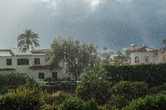 Heavy rain falling on white Mediterranean houses and palm trees in Spain during a storm