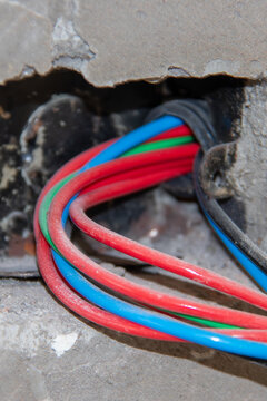 Curved colored electrical wires passing through a metal wall junction box. Focus on electrical infrastructure, wiring, construction, and electrician.