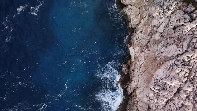 Aerial cliff edge with crashing surf wave exposed limestone ledges filmed by drone from above. Deep blue water with foamy breakers splashing onto rock. Amazing seascape in Turkey. Nature theme