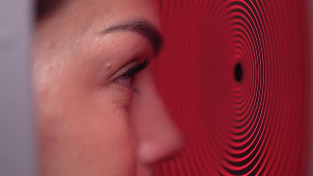 Woman undergoes computerized eye diagnostics using an autorefractor with a red optical pattern. Concept vision screening and ophthalmic technology.