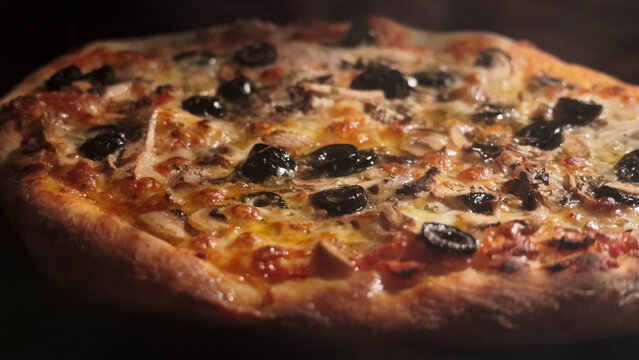 Freshly baked artisanal pizza with melted cheese, black olives, and mushrooms inside a warm oven