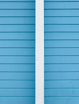 Vertical white post centered against horizontal bright blue wooden siding
