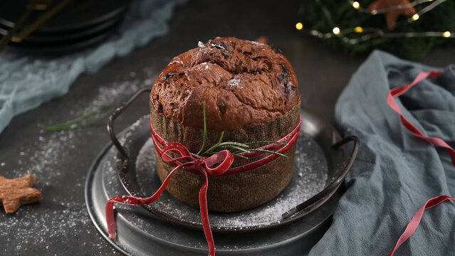 Chocolate panettone cake tied with a red ribbon and decorated for the holidays on a metal tray