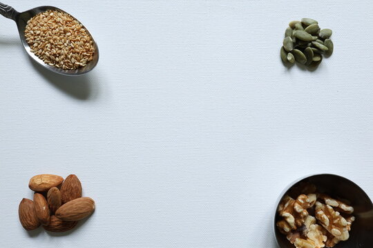 Flat lay of sesame seeds, pumpkin seeds, almonds and walnuts framing a white background with generous copy space for healthy food and nutrition designs.