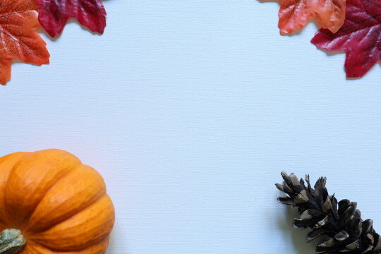Orange pumpkin, pine cone and red and orange autumn leaves frame a white background with generous copy space for seasonal and harvest designs.