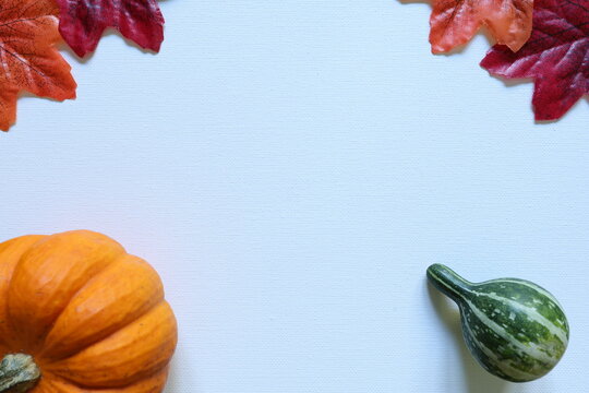 Orange pumpkin, green decorative gourd and autumn leaves frame a white background with generous copy space for harvest and seasonal designs.
