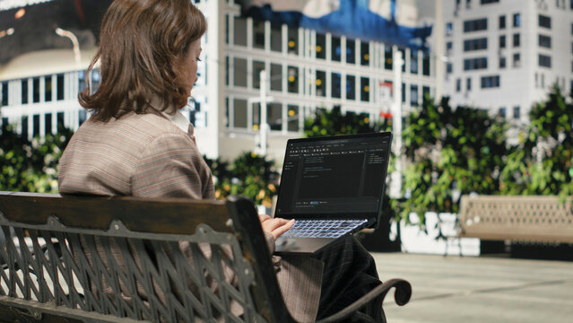 Programmer writing code on laptop while sitting on park bench outdoors