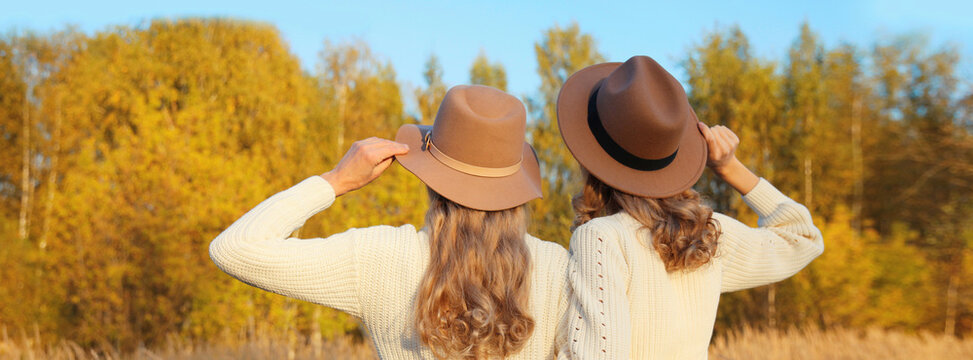 Two women friends together in autumn park, stylish girlfriends in hat, trees with yellow leaves