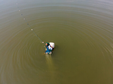 Aerial view of a fisherman wearing a traditional conical hat while casting a net in the waters of Toyareja, Purbalingga, Central Java, Indonesia.