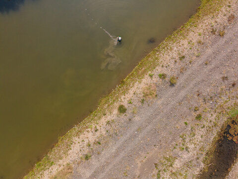 Aerial view of a fisherman standing in the water of Toyareja river with a gravel bank along the shore in Purbalingga, Central Java, Indonesia.