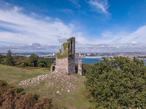 Aerial view of the Folly ruin at Mount Edgcumbe, featuring stone walls and ivy, set against a backdrop of the sea and coastline in Cremyll, England, United Kingdom.