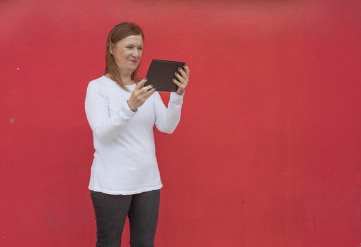 Focused mature woman using digital tablet against vibrant red background