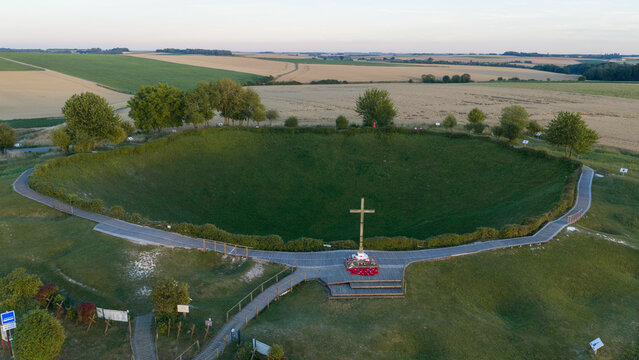 Aerial view of Lochnagar Crater, a historic WW1 explosion crater with a wooden cross memorial, surrounded by grassy slopes and walking paths in Ovillers-la-Boisselle, Hauts-de-France, France.